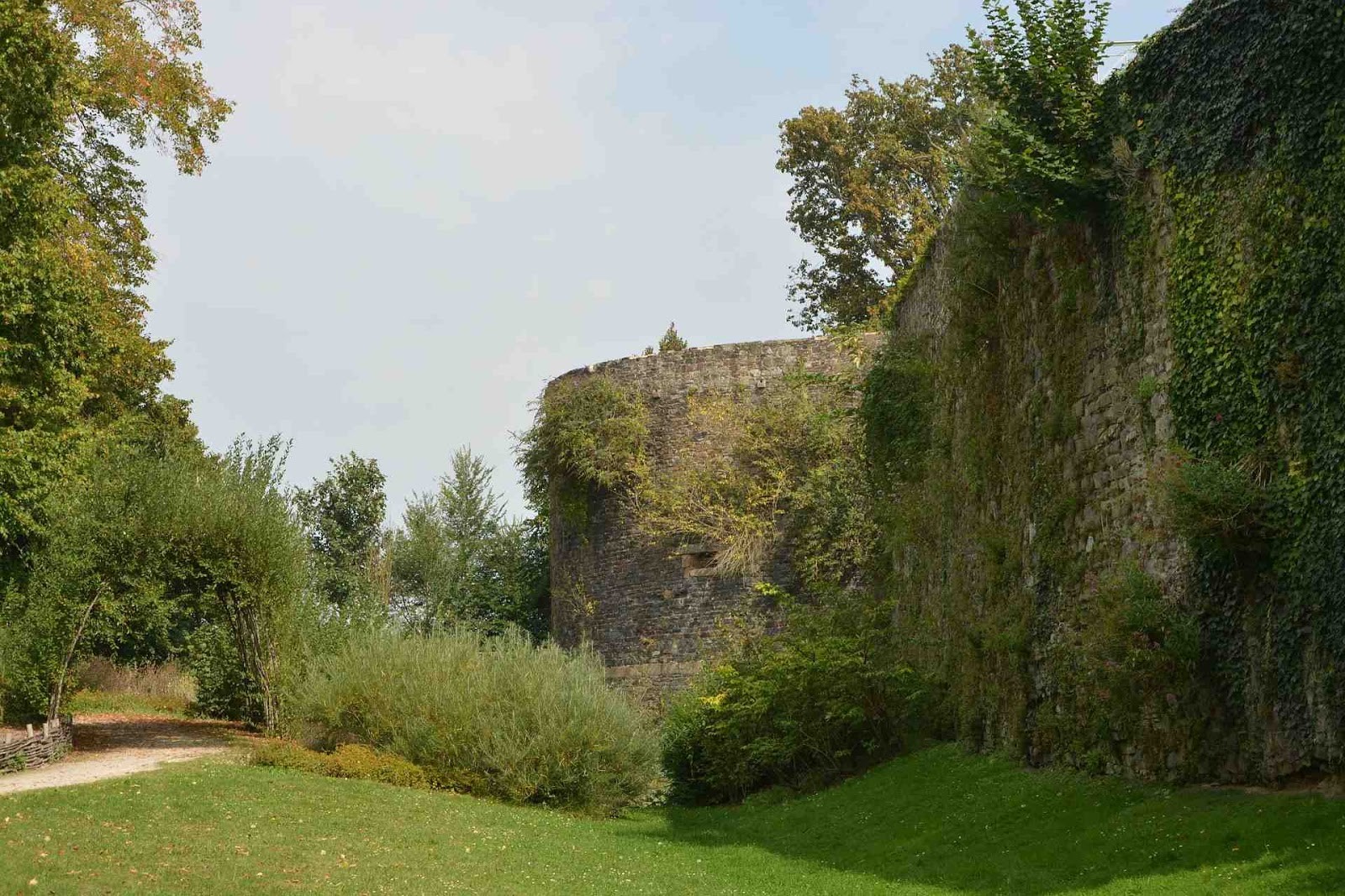 Sur la gauche, une chemin s’enfonce dans la végétation. Sur la droite, les remparts de la ville de Dol-de-Bretagne.