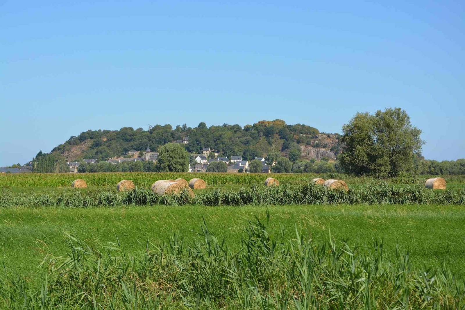 La photo est prise dans un champ. Au loin est visible un village surplombé par un relief haut de 60 mètres et long de plusieurs centaines de mètres.