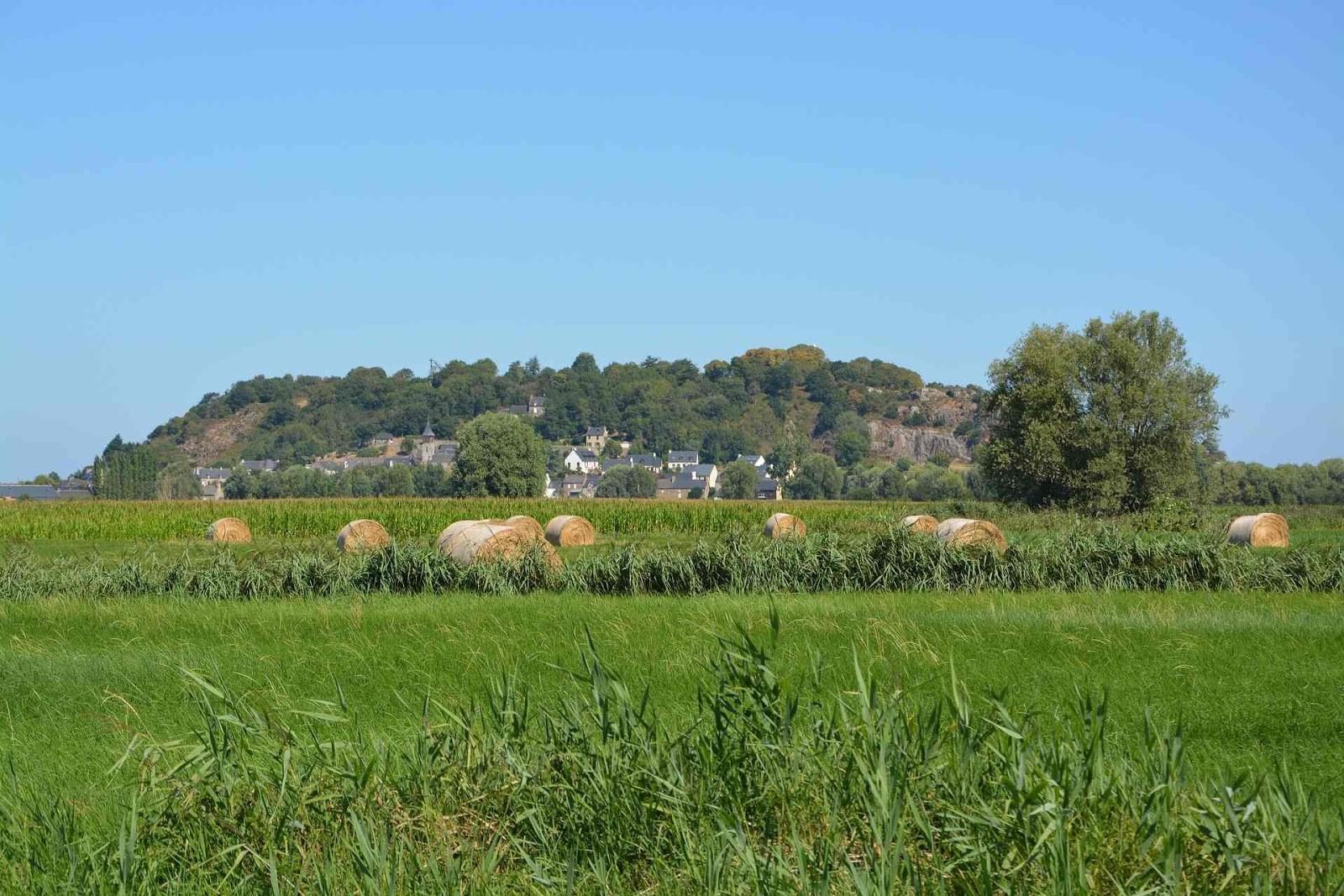  La photo est prise dans un champ. Au loin est visible un village surplombé par un relief haut de 60 mètres et long de plusieurs centaines de mètres.