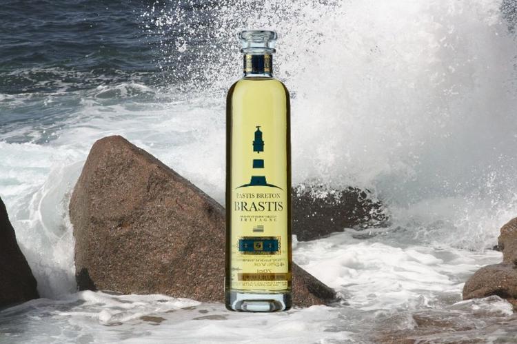 Bouteille de Brastis, le pastis breton, sur fond de la mer et d'une vague frappant un rocher