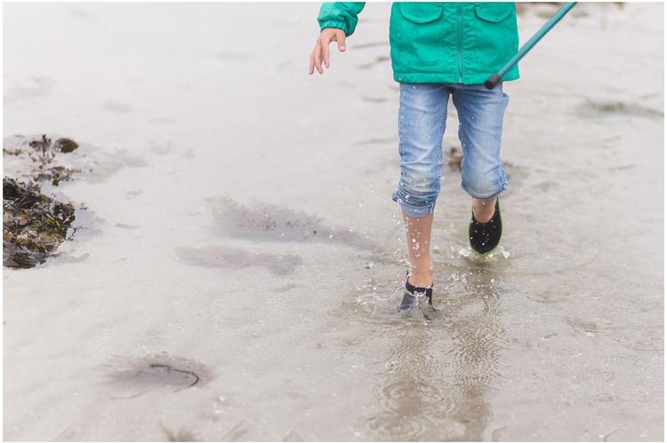 Un enfant au manteau vert marche dans l'eau de mer sur une plage bretonne .
