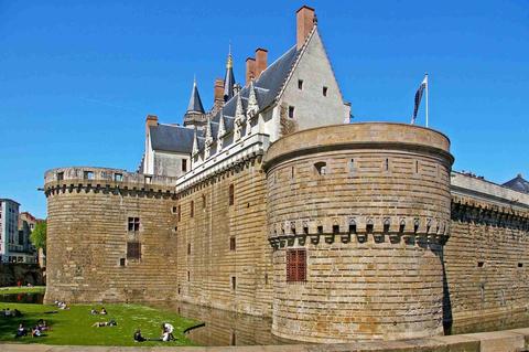 Le château des ducs de Bretagne vu de l’extérieur. A gauche, des gens se relaxent dans l’herbe. Au premier plan, le château fort entoure le logis de la cour intérieure dont on voit le toit en arrière plan.